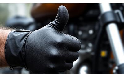 Close-up of a hand with a biker glove giving a thumbs up in front of a motorcycle engine.